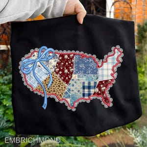 Op de afbeelding: Zwarte draagtas met een patchwork-ontwerp in de vorm van de Verenigde Staten. Het patchwork bevat verschillende bloemen- en ruitpatronen in rood, blauw en crème. Een blauwe strik en kanten rand omlijsten het ontwerp. De tekst "EMBRICHMOND" staat onderaan.