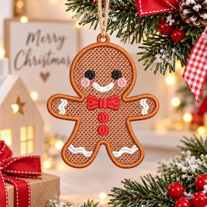 May include: A brown gingerbread man ornament featuring embroidered details including black eyes, pink cheeks, a white smile, a red bow tie, and two red buttons. The ornament has white icing-style trim on the arms and legs and a jute string loop.