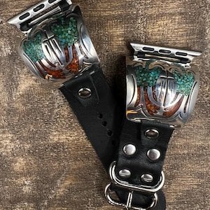 May include: Two watch bands with silver-toned metal accents and black leather straps. The metal features turquoise and red stone inlays. The bands are designed to fit a smartwatch and have a buckle closure.
