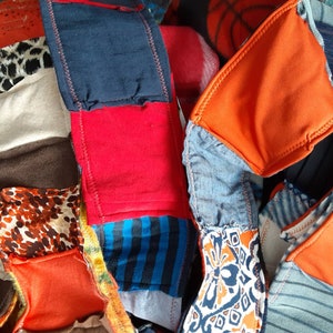 May include: A patchwork textile item composed of various fabrics, including denim, orange, red, and patterned materials. The design features a mix of textures and colors, with visible stitching.