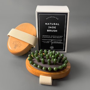 Può includere: Una spazzola naturale in giada di legno con cinturino beige e scatola. La spazzola ha pietre di giada verdi ed è progettata per migliorare la circolazione e il drenaggio linfatico. La scatola riporta la scritta "Natural Jade Brush".