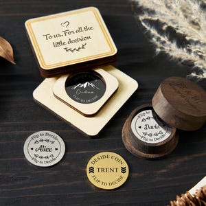 Puede incluir: Cajas de recuerdo de madera y monedas de decisión con texto grabado. Las cajas tienen el texto "To us. For all the little decision" y "Who Will Decide?". Las monedas dicen "Alice", "Trent" y "David", con el texto "Flip to Decide".