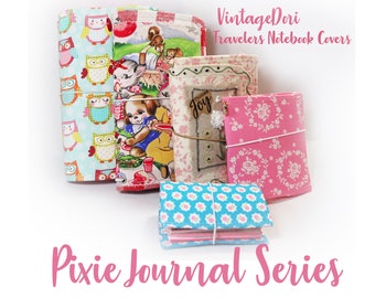 May include: Five different fabric-covered notebooks with elastic closures. The covers feature various patterns, including owls, a picnic scene, a floral design, and a design with the word "Joy". The notebooks are labeled "VintageDori Travelers Notebook Covers Pixie Journal Series".