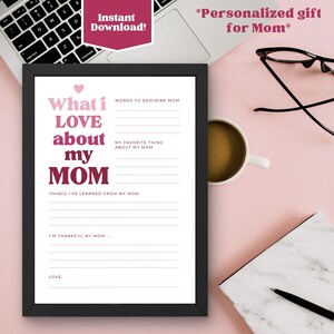 K&ouml;nnte beinhalten: Ein gerahmter Druck mit dem Text "What i LOVE about my MOM" in Rosa und Wei&szlig;. Der Druck enth&auml;lt Ausf&uuml;llfelder f&uuml;r W&ouml;rter zur Beschreibung von Mama, Lieblingsdinge und gelernte Dinge. Ein Laptop, eine Kaffeetasse und eine Brille sind im Hintergrund.