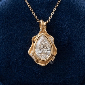 May include: A gold pendant necklace featuring a large pear-shaped center stone surrounded by a fluid, organic-shaped gold frame accented with small round diamonds. The pendant hangs from a delicate gold chain, showcasing a polished metal finish.