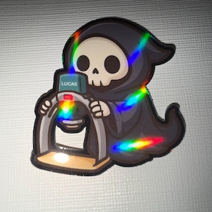 May include: A sticker featuring a cartoon Grim Reaper character in a black hooded cloak, holding a microscope. The microscope has the name "LUCAS" on it. The sticker has a holographic rainbow effect.
