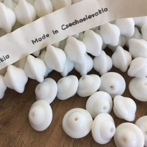 May include: A collection of white glass beads with a domed top. The beads are labeled "Made in Czechoslovakia".
