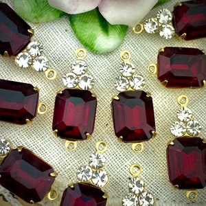 Peut inclure: Une collection de breloques pendantes en verre rouge avec des montures dorées et des accents de strass transparents. Chaque breloque présente une pierre en verre rouge rectangulaire avec un design facetté.