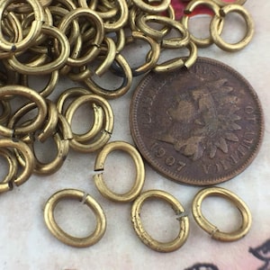 Könnte beinhalten: Ein Haufen ovaler Messing-Sprünge, einige sind offen und einige sind geschlossen. Die Sprungringe liegen neben einer US-Cent-Münze aus dem Jahr 1907.