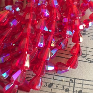 May include: A strand of red iridescent glass beads. The beads are faceted and have a teardrop shape.