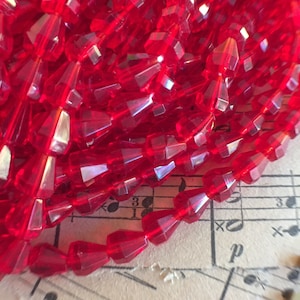 May include: A strand of red faceted glass beads. The beads are shaped like teardrops and have a shiny, iridescent finish.
