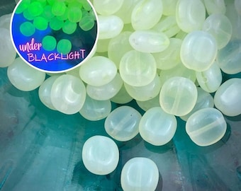 Könnte beinhalten: Ein Haufen blassgrüner Glasperlen. Die Perlen sind rund und flach und haben eine glatte, polierte Oberfläche. Die Perlen werden unter Schwarzlicht gezeigt und leuchten in einem leuchtenden Grün.