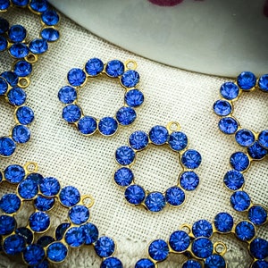 May include: A close-up of blue rhinestone embellishments with gold settings. The rhinestones are arranged in a circular pattern, creating a decorative design.