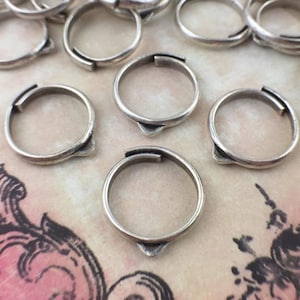 May include: A group of silver-toned metal rings with a pointed edge. The rings are arranged on a textured surface.