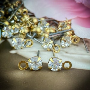 May include: A pair of gold-tone earring findings with clear crystal rhinestones. The findings have a small loop on the top for attaching to a larger earring.