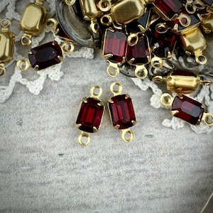 May include: Two gold-toned connector pieces with red glass stones. The connector pieces have two loops on each side. The stones are rectangular and have a faceted cut.