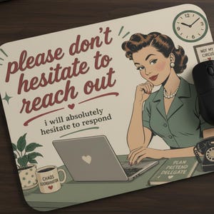May include: A rectangular mousepad with a retro illustration of a woman at a desk. The mousepad has the text "please don't hesitate to reach out, I will absolutely hesitate to respond." A black mouse and keyboard are visible.