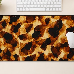 May include: A rectangular mouse pad with a tortoiseshell pattern in shades of brown, black, and cream. A white computer mouse rests on the right side of the pad. A white keyboard and a cup are in the background.