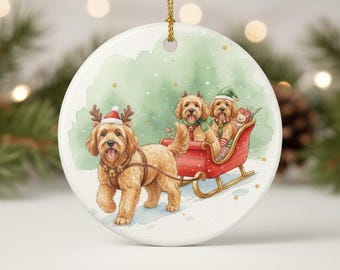 May include: A round Christmas ornament featuring a watercolor illustration of three dogs in a red sleigh. One dog, wearing a Santa hat and reindeer antlers, pulls the sleigh. The other two dogs are in the sleigh, wearing festive hats and scarves.