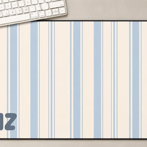 May include: A rectangular mouse pad with a cream background and vertical light blue stripes. The letters "ANZ" are in the lower left corner. A white keyboard and mouse are visible.