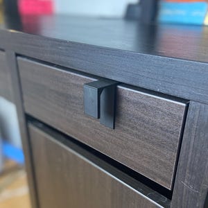 May include: Close-up of a dark wood cabinet with a black metal handle. The cabinet has two drawers with a wood grain texture. The handle is a simple, modern design.