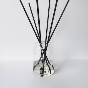 May include: A clear glass diffuser bottle with black reeds. The bottle has a silver and black label that reads "LUMI SCENTS CHESHIRE". The reeds are arranged in a fan shape, and the liquid inside the bottle is visible.