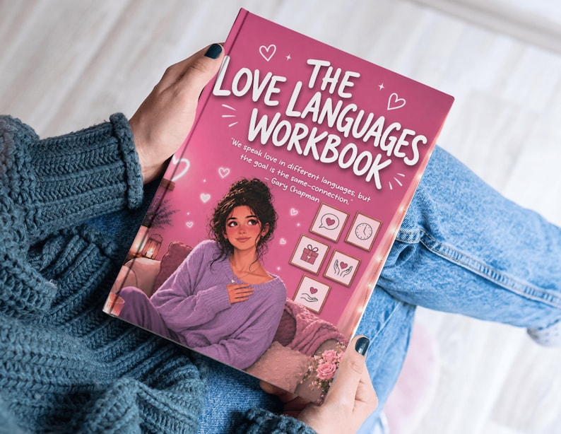 May include: A pink workbook titled "The Love Languages Workbook" with a cartoon illustration of a woman on the cover. The woman is wearing a purple outfit and sitting on a couch. The book is being held by a person wearing a blue sweater and jeans.