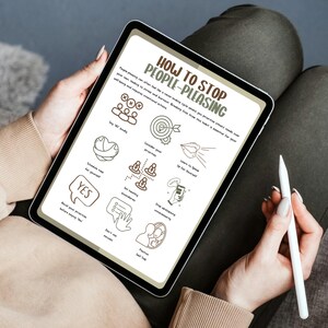 May include: A person holding a tablet displaying a guide titled "How to Stop People-Pleasing." The screen shows hand-drawn illustrations and text. A white stylus is held in the person's other hand. The person is wearing a beige sweater and sitting on a dark surface.