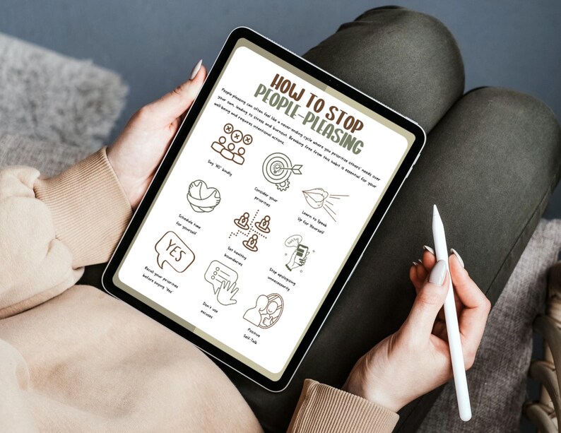 May include: A person holding a tablet displaying a guide titled "How to Stop People-Pleasing." The screen shows hand-drawn illustrations and text. A white stylus is held in the person's other hand. The person is wearing a beige sweater and sitting on a dark surface.