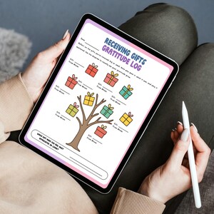 May include: A digital tablet displaying a "Receiving Gifts Gratitude Log." The log features a tree with colorful gift boxes and prompts for recording gift details. A stylus rests in the hand, suggesting digital note-taking. The tablet is held on a person's lap.