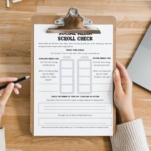 May include: A clipboard with a printed "Social Media Scroll Check" form, featuring sections for tracking energy levels and reflection. A hand holds a pencil, ready to fill out the form. A laptop is visible in the background.