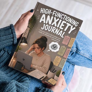 May include: A journal titled "HIGH-FUNCTIONING ANXIETY JOURNAL" is held open. The cover illustration depicts a woman at a desk with a laptop, looking stressed. The journal's text reads, "I function well on the outside, but inside I'm constantly overthinking everything."