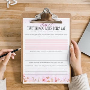 Pu&ograve; includere: Un appunti con un foglio di lavoro stampato intitolato "Trusting God After Betrayal". Il foglio di lavoro ha linee rosa e accenti floreali. Una mano tiene una matita, pronta per scrivere. Un laptop e auricolari sono sullo sfondo.