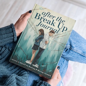 May include: A journal titled "After the Break Up Journal" is held in a person's hands. The cover art depicts a couple standing back-to-back with a teal and white background. The text "Letters to Myself on Healing & Moving Forward" is at the bottom.