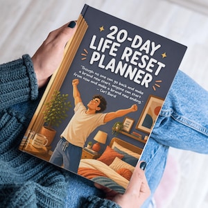 Op de afbeelding: Een persoon die een 20-Day Life Reset Planner vasthoudt. De omslag toont een cartoonillustratie van een persoon met opgeheven armen in een slaapkamer. De titel van de planner is in het wit, met een citaat van Carl Bard.