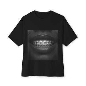 Puede incluir: Foto en blanco y negro de una boca con brackets. La foto está impresa en una camiseta negra.