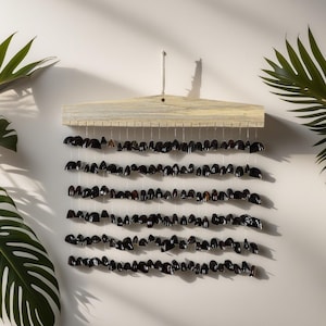 Może przedstawiać: Dekoracja ścienna z rzędami ciemnobrązowych, błyszczących elementów w kształcie łezki zawieszonych na jasnej drewnianej listwie. Elementy są nawleczone na cienkie, przezroczyste sznurki, tworząc warstwowy efekt.