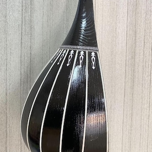 Może przedstawiać: Czarny instrument strunowy z białymi akcentami. Instrument ma gruszkowaty korpus z pionowymi białymi paskami i dekoracyjnymi białymi wzorami w pobliżu szyjki. Widoczne usłojenie drewna, instrument ma błyszczące wykończenie.