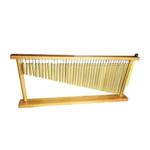 May include: A wooden wind chime instrument with numerous gold-colored metal tubes suspended from a wooden frame. The tubes are arranged in a descending diagonal pattern. A black ball is on the right side of the frame.
