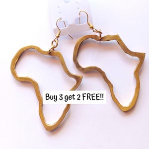 May include: Gold-colored earrings in the shape of the African continent. The earrings are hanging from a white tag. The text "Buy 3 get 2 FREE!!" is displayed on the image.