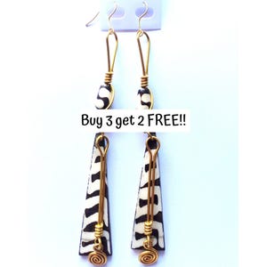 May include: A pair of dangle earrings with a black and white zebra print design. The earrings have gold-colored wire accents and a spiral design at the bottom. The text "Buy 3 get 2 FREE!!" is visible.