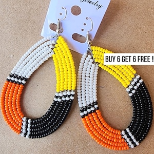 May include: A pair of beaded teardrop earrings. The earrings feature a color block design with white, yellow, orange, and black beads. The text "BUY 6 GET 6 FREE !" is visible on the tag.