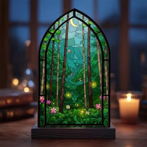 May include: A stained glass window depicting a forest scene with tall trees, a crescent moon, and fireflies. The window is set in a black frame and sits on a wooden base. Pink and white flowers are at the bottom of the window.