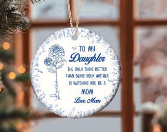 May include: A white ceramic ornament with a blue floral design and the text "TO MY Daughter THE ONLY THING BETTER THAN BEING YOUR MOTHER IS WATCHING YOU BE A MOM Love, Mom". A gold chain is attached for hanging.
