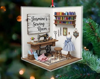 May include: A decorative ornament featuring a miniature sewing room scene. The scene includes a sewing machine, dress form, spools of thread, and the text "Jasmine's Sewing Room". The ornament is designed to hang with a red ribbon.