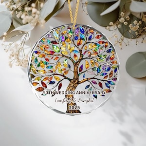 Könnte beinhalten: Ein klarer, runder Ornament mit einer goldenen Kette. Das Ornament zeigt ein farbenfrohes Baumdesign mit einem braunen Stamm und lebendigen Blättern in Rot-, Gelb-, Blau- und Lilatönen. Der Text am unteren Rand lautet "50. HOCHZEITSTAG" sowie Namen und das Jahr 2025.