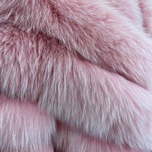 May include: Close-up of a luxurious pink fur texture. The fur appears soft and fluffy, with long, flowing strands in varying shades of pink and white. The image highlights the texture and depth of the fur.