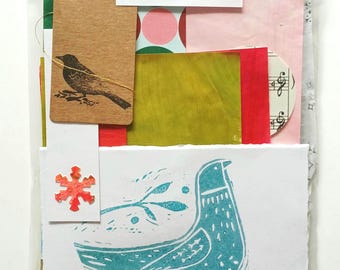 Pode incluir: Um pacote de papel misto numa manga de plástico transparente com uma etiqueta que diz PAPER SQUIRREL STORE mixed PAPER PACK handmade found rescued. Inclui uma etiqueta castanha com um pássaro preto, um floco de neve vermelho e um cartão branco.