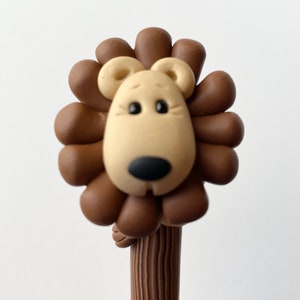 May include: A brown and tan lion head pencil topper with a brown wooden pencil.