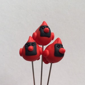 May include: Three handmade red cardinal bird ornaments with black facial markings and red beaks. The birds are mounted on silver-colored metal stems, perfect for floral arrangements or holiday decor.